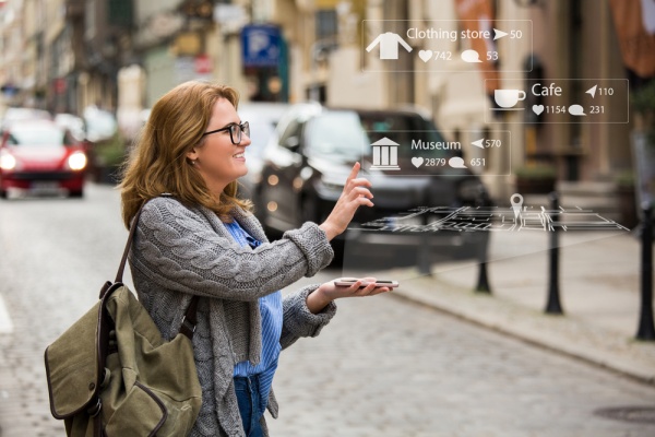 Esempio applicativo di realtà aumentata: immagine che mostra una donna che fruisce di contenuti digitali in maniera "aumentata" direttamente dal proprio smartphone vedendo proiettato nello spazio reale una mappa digitale che illustra i luoghi vicini